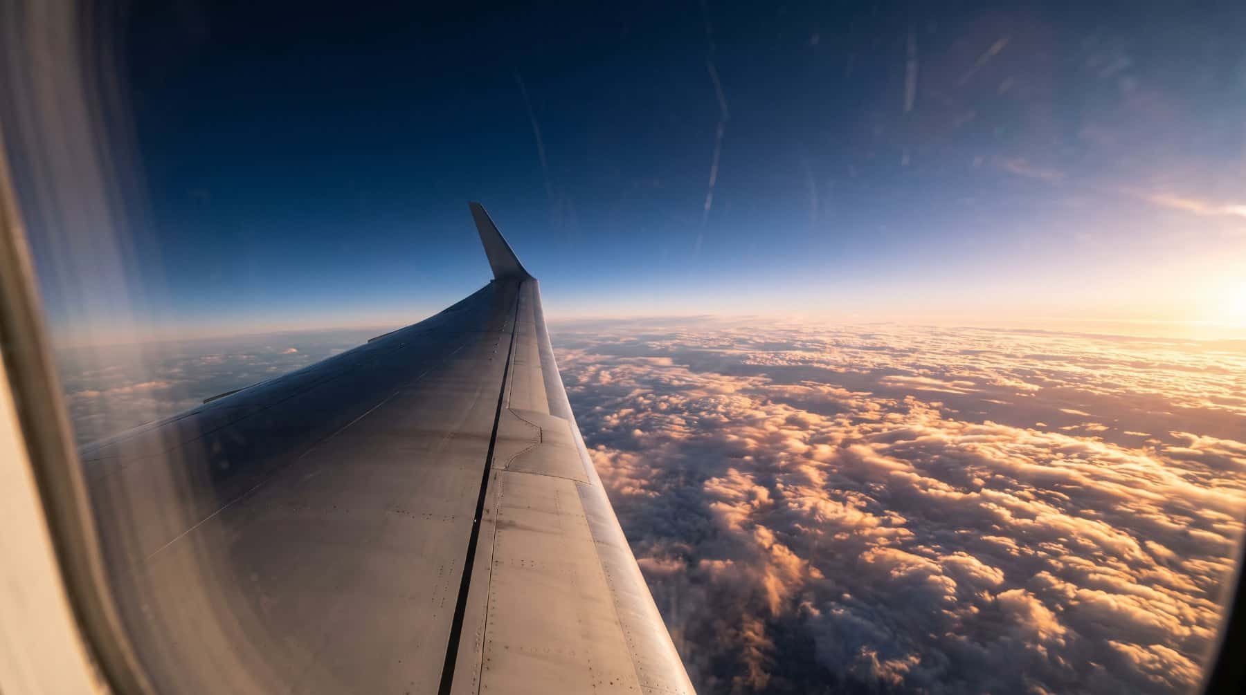 Airplane wing above a sunlit sea of clouds seen from a window seat