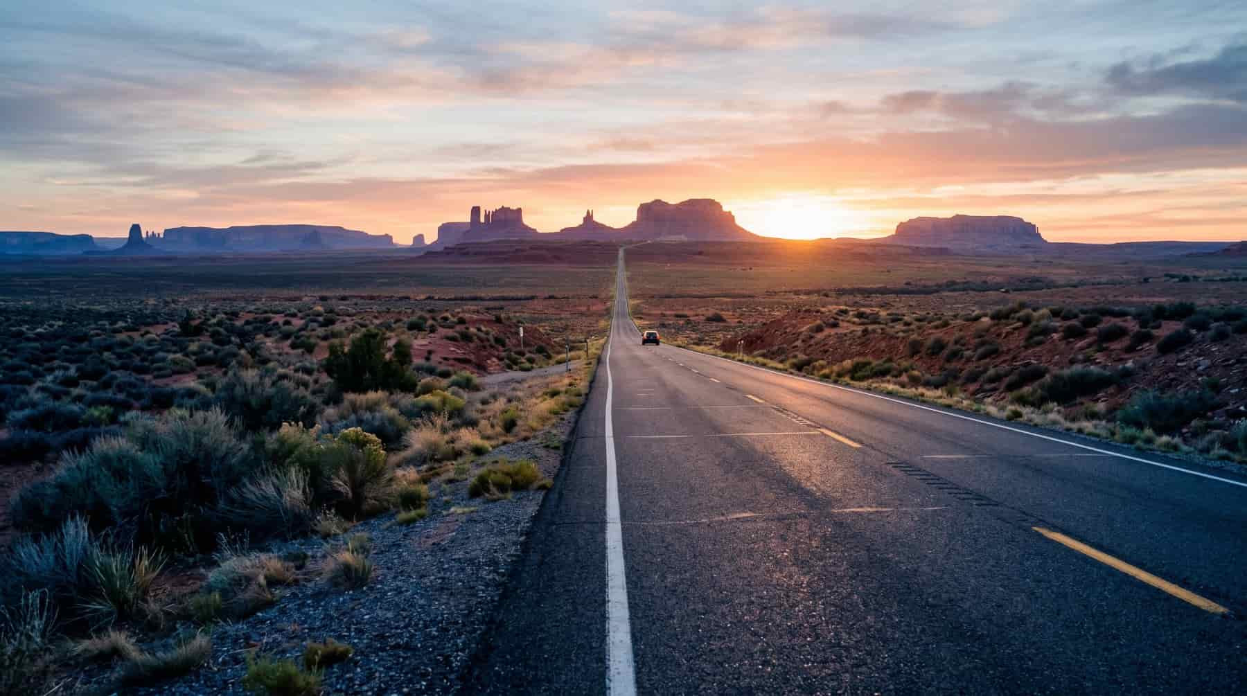 Empty desert highway leading toward sandstone buttes at sunrise
